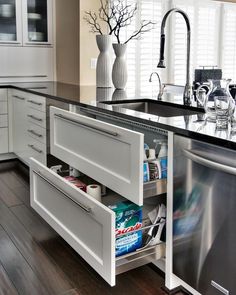 an open drawer in the middle of a kitchen counter with bottles and cans on it