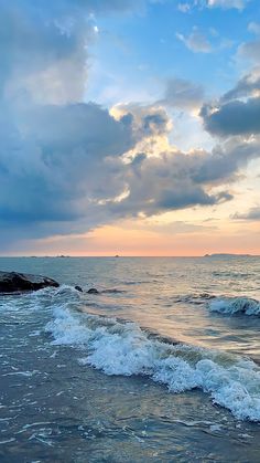 the sun is setting over the ocean with waves crashing on the shore and clouds in the sky