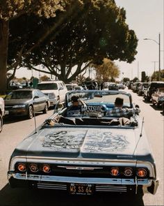 an old car with graffiti on the hood parked in front of a tree lined street