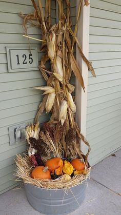 a bucket filled with corn and pumpkins next to a house number sign on the front door