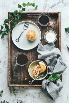 a wooden tray topped with two plates of food and cups of coffee next to each other