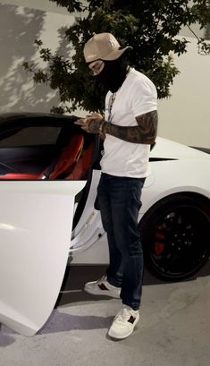 a man standing next to a white sports car with the hood up and his hand on the door