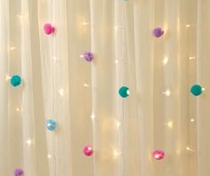 the curtain is decorated with pom - poms and string lights for a festive touch