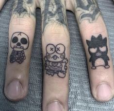 two fingers with tattoos on them, one has a skull and the other has a cat