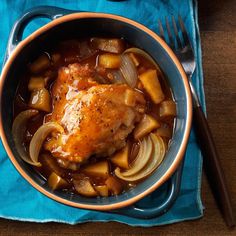 a chicken dish with onions and carrots in a blue bowl next to a fork