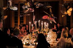 a group of people sitting around a dinner table with candles and butterflies flying above them