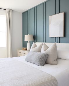 a bed with white linens and pillows in front of a blue paneled wall