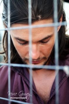 a man with long hair looking down at his cell phone in a caged area