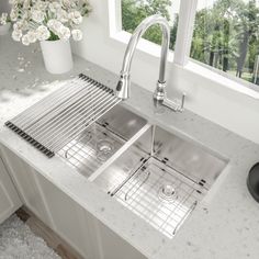 a stainless steel kitchen sink with grid strainers on the front and side, under a window