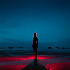 a woman standing on top of a beach next to the ocean under a blue sky