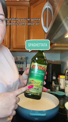 a woman holding a bottle of extra virgin olive oil in her hand and pointing at it