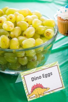 a bowl filled with grapes next to cupcakes on top of a green table