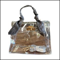 This sophisticated bag gives a nod to the iconic Kelly bag. Available with several different gameday colored twillies, the Andrea Bag measures 9.5 inches x 7 inches 4 inches. Gold hardware come with a clear cross body strap. Trendy Crossbody Satchel With Clear Strap, Clear Rectangular Bag With Detachable Strap, Trendy Clear Crossbody Satchel, Trendy Clear Satchel For Shopping, Trendy Clear Bags For On-the-go, Chic Rectangular Satchel With Clear Strap, Chic Clear Bag With Detachable Strap, On-the-go Rectangular Shoulder Bag With Clear Strap, Chic Clear Bags With Detachable Strap