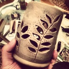 a person holding up a cup made out of clay with holes in the middle and leaves on it