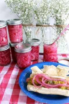 a plate with a sandwich on it next to jars of pickled onions and tortillas