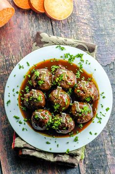 meatballs covered in gravy and garnished with parsley on a white plate