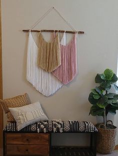 two wall hangings are hung on the wall next to a bench with pillows and a potted plant