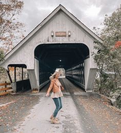 a woman standing in front of a covered bridge on a fall day with leaves all over the ground