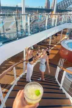 two women standing on the deck of a cruise ship with drinks in their hand and one woman holding up a drink