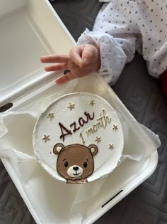 a baby's hand reaching for a cake with a teddy bear design on it