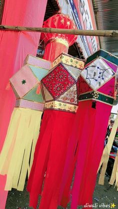 some colorful umbrellas hanging from a wooden pole in front of a building with red curtains