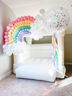 an inflatable rainbow arch with balloons and streamers on the floor next to it