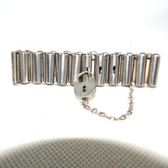 A Victorian sterling bracelet made out of a series of  long curved links held together with wire ovals. The last couple of long links have holes in them which a small loop on the last wire link fits through.  A padlock fits through this loop to hold the bracelet closed. The padlock has a keyhole in it but it is just decorative and is attached to the body of the bracelet with a chain so it can't get lost. The padlock is opened simply by pressing and pulling on the latch side of the hasp. This bra Silver Oval Link Bracelet With Box Clasp, Silver Bracelets With Hook And Links For Formal Occasions, Sterling Silver Formal Bracelet With Hook And Links, Silver Chain Bracelet With Rectangular Links And Box Clasp, Silver Link Chain Bracelet With Box Clasp, Heart Padlocks, Reverse Painted, Sterling Bracelets, Rhinestone Bracelet