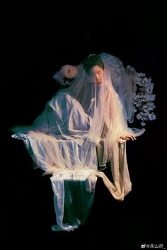 a woman in white dress and veil laying on the ground with flowers around her head