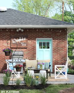 an outdoor patio with chairs, table and grill in front of a brick building that has a blue door