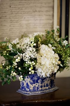 a blue and white vase filled with lots of flowers on top of a wooden table