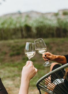 two people toasting with wine glasses on a patio table outside in the grass,