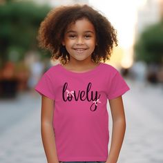 This adorable coquette-style t-shirt is perfect for little fashionistas, featuring a sweet "Lovely" script surrounded by delicate pink bow accents. Made from soft, breathable fabric, it's both stylish and comfortable for everyday wear. The kids heavy cotton tee is perfect for everyday use. The fabric is 100% cotton for solid colors. Polyester is included for heather-color variants. The shoulders have twill tape for improved durability. The collar is curl resistant due to ribbed knitting. There a Summer Pink T-shirt With Cute Design, Playful Pink Tops With Cute Design, Sweet Pink Tops With Letter Print, Cute Cotton T-shirt With Pink Bow, Pink T-shirt With Bow For Summer, Cute Pink Tops For Gifts, Cute Pink Top As Gift, Cute Pink Tops For Gift, Cute Cotton Tops With Pink Bow