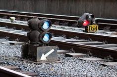 two traffic lights sitting on top of train tracks next to each other with an arrow pointing in the opposite direction