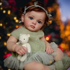 a baby girl holding a teddy bear in front of a christmas tree with lights behind her