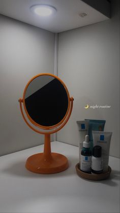 an orange mirror sitting on top of a table next to a cup and bottle of lotion