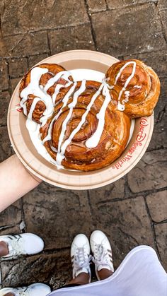 a person holding a plate with pastries on it and white icing drizzles