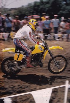 a man riding on the back of a yellow dirt bike in front of a crowd