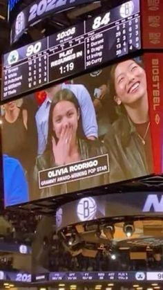 the scoreboard at an indoor basketball game shows two young women laughing and looking up