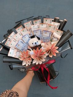 a hand holding a bouquet of money with a teddy bear on it