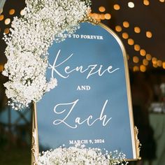 a wedding sign with baby's breath flowers on it and lights in the background