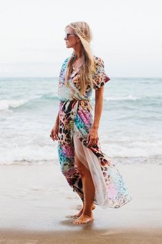 a woman standing on top of a beach next to the ocean wearing a colorful dress