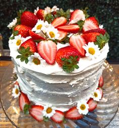 a white cake with strawberries and daisies on the top is sitting on a glass platter