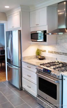 a stainless steel refrigerator and stove in a kitchen with marble counter tops, white cabinets and tile flooring