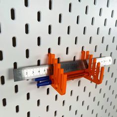 there is a ruler on the wall with holes in it and two orange plastic pegs