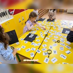 a group of children sitting around a yellow table with scissors and letters on the table