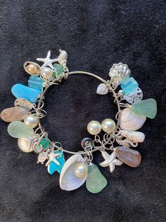 "Kingman Turquoise Ocean Jasper Sea shells beach glass Pearls and Sterling plated beach charms on a bangle charm bracelet. With Ocean Jasper, 6 Pearls, 2 Sea shells, 6 pieces of beach glass, 12 beach charms, 3 hand blown glass beads, 1 Petoskey stone, a piece of Kingman Turquoise and 2 blue glass beads finish this bangle charm bracelet.   The bangle bracelet is  2.5\" inches in width. See all my charm bracelets here: https://www.etsy.com/shop/MoonwaterJewelryShop?section_id=34394213 All my bracelets are different and would be considered one of a kind. View my collection of Kingman Arizona Turquoise here: https://www.etsy.com/shop/MoonwaterJewelryShop?section_id=28192591  I've been selling on eBay since 2003 Came to Etsy to sell jewelry. Returns and exchange details ► RETURNS / EXCHANGES Al Shell Charm Bracelet, Beach Glass Nails, Sea Glass Bangle, Beach Charms Bracelet Jewelry, Bohemian Beach Bracelets With Charms, Bohemian Charm Bracelets For The Beach, Beach Ocean-inspired Charm Bracelet, Bohemian Charm Bracelet For Beach With Lobster Clasp, Handmade Charm Bangle For Beach