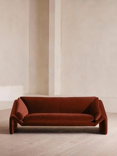 a red couch sitting on top of a hard wood floor next to a white wall