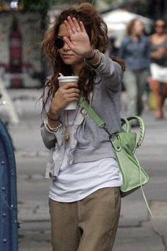 a woman walking down the street holding her hand up to her face