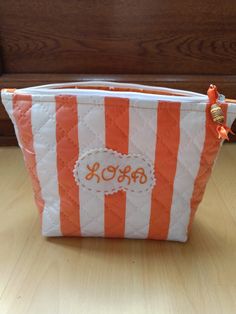 an orange and white striped cosmetic bag with monogrammed initials on the front pocket