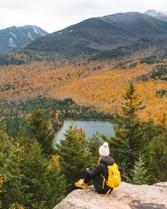 a person sitting on top of a rock looking out over a valley and lake in the distance